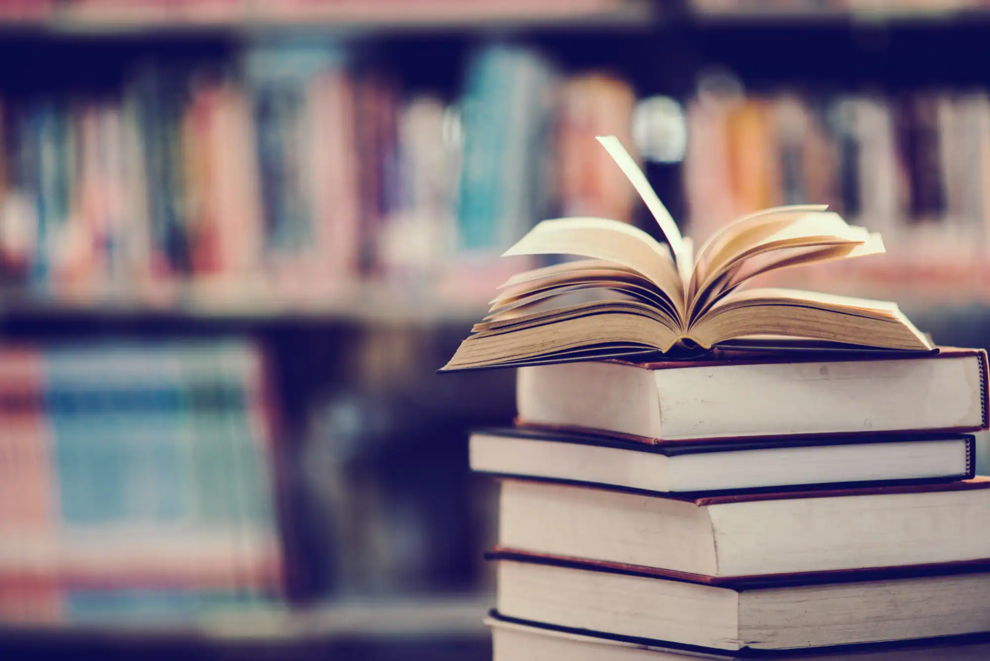 Open book resting on a stack of books in a library, representing publications and research.