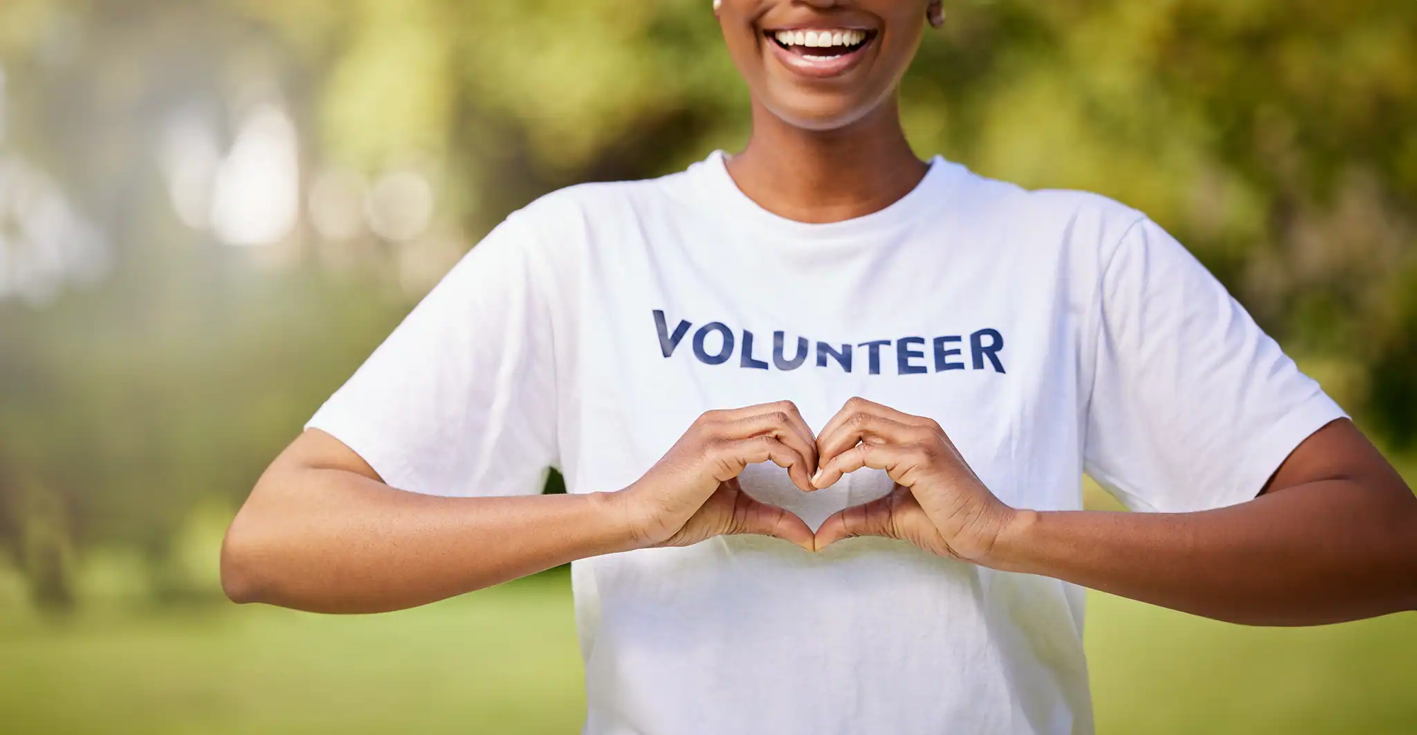 A person wearing a volunteer t-shirt doing a heart symbol with her hands.