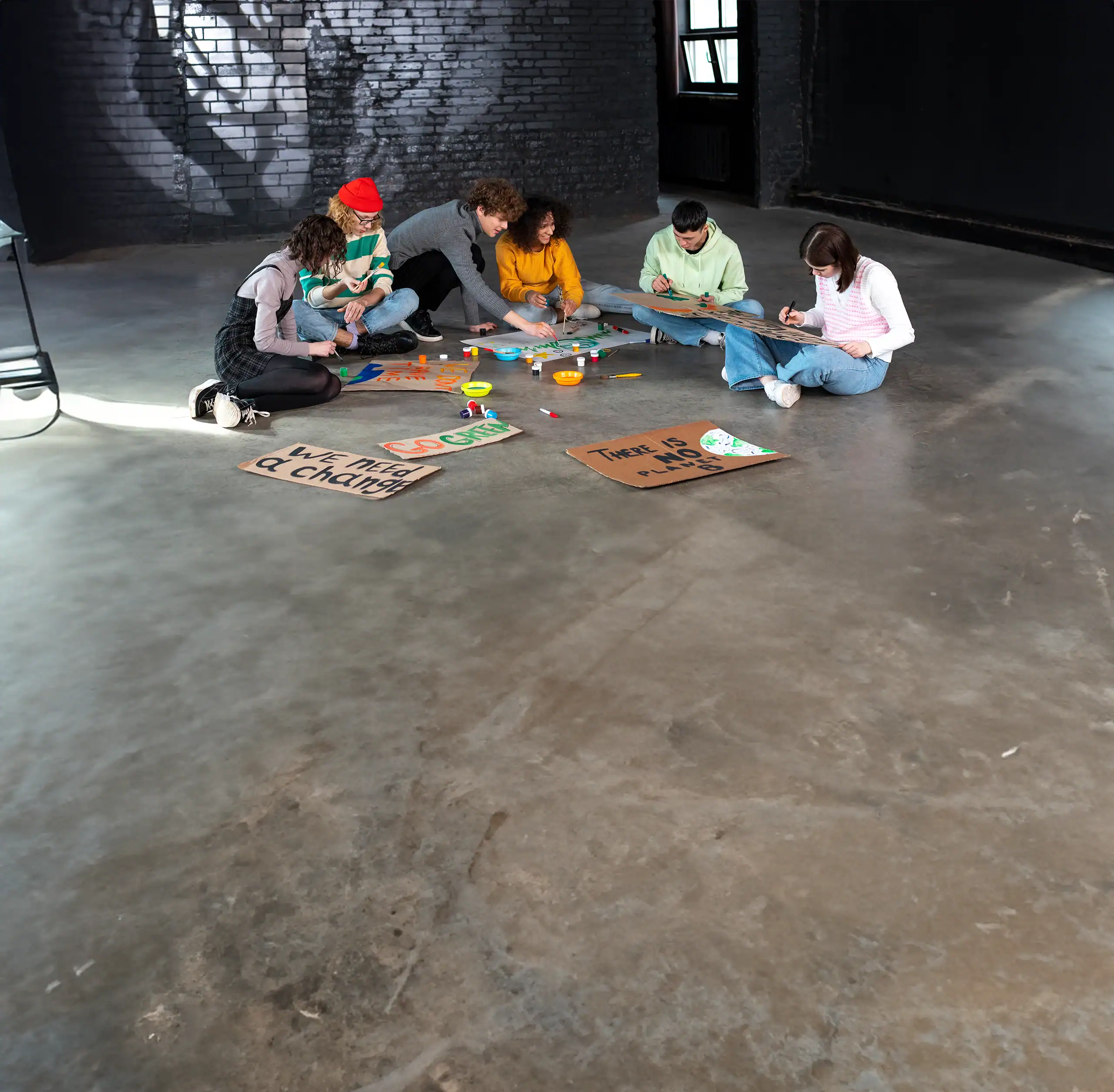 Young people sitting together on a concrete floor making protest-style posters, representing resilience and inclusion.